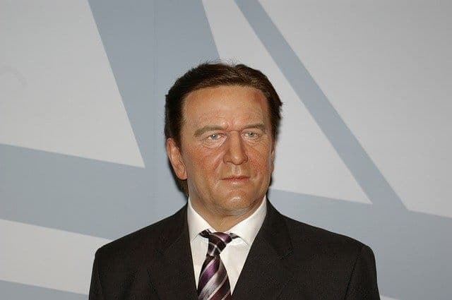 A man in a dark suit and tie photographed against a plain grey backdrop